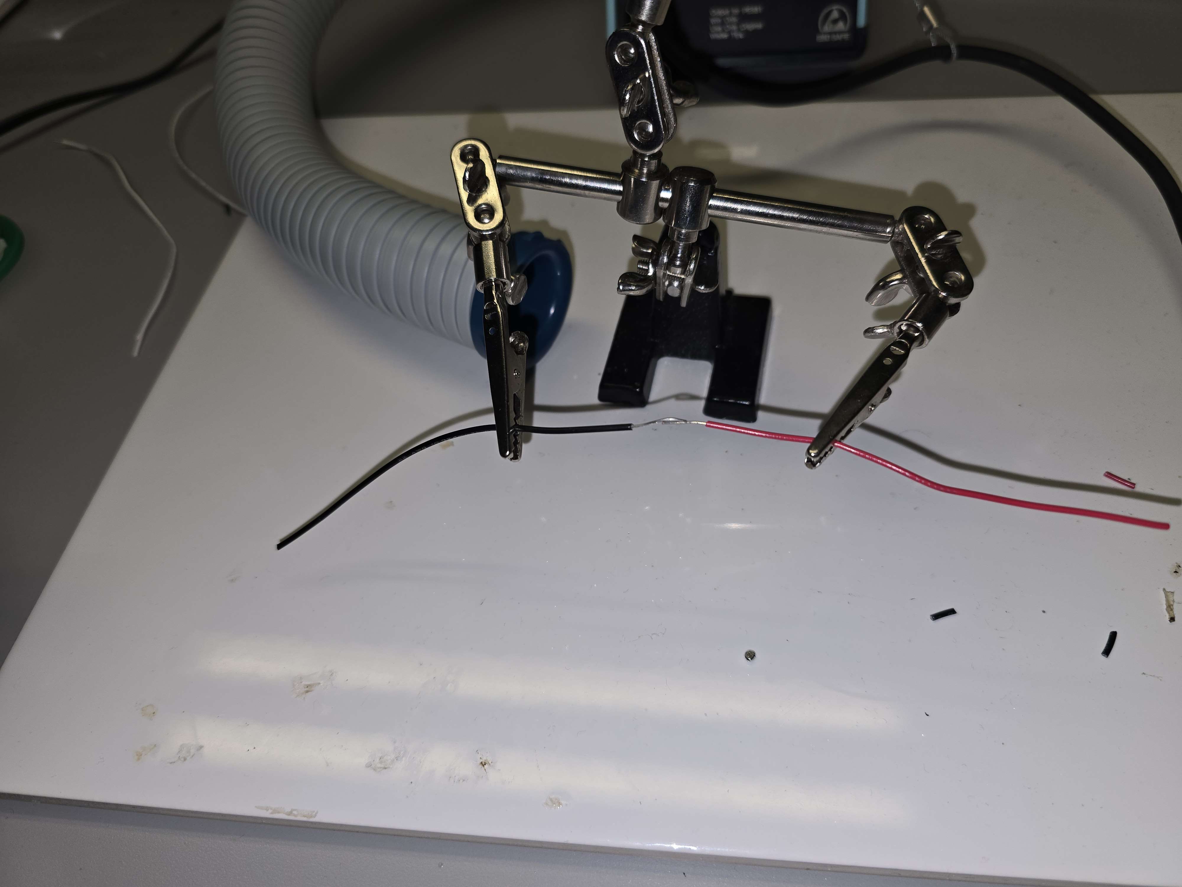 Helping hands holding red and black wires for soldering